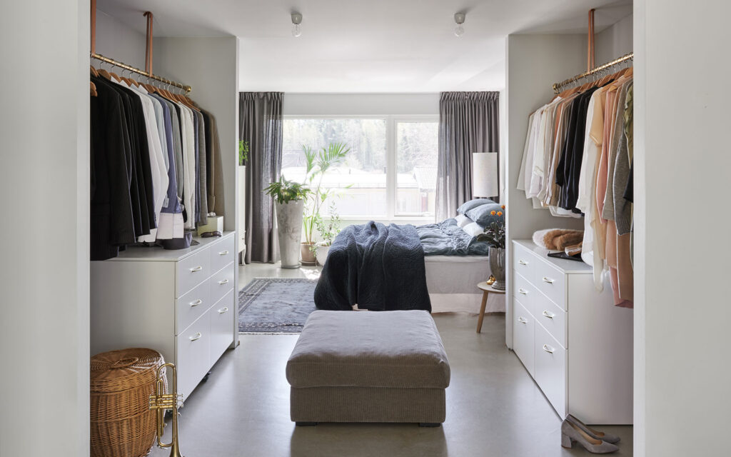 Heads and tails 5 Elegant passage in i sovrummet genom öppen ljus garderob. På golvet, en grå sittbänk. Bakom, sängen och grå gardiner i linne.