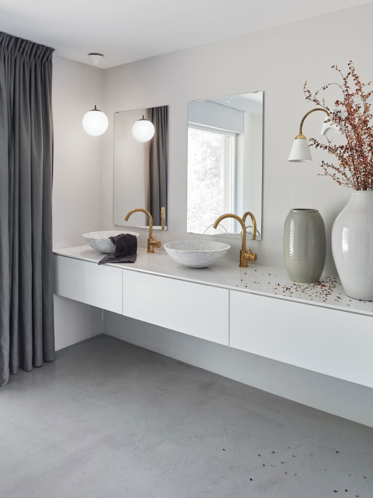 Heads and tails 4 Minimalistiskt badrum med vit inredning, guldaccentkranar och eleganta hängande lampor.