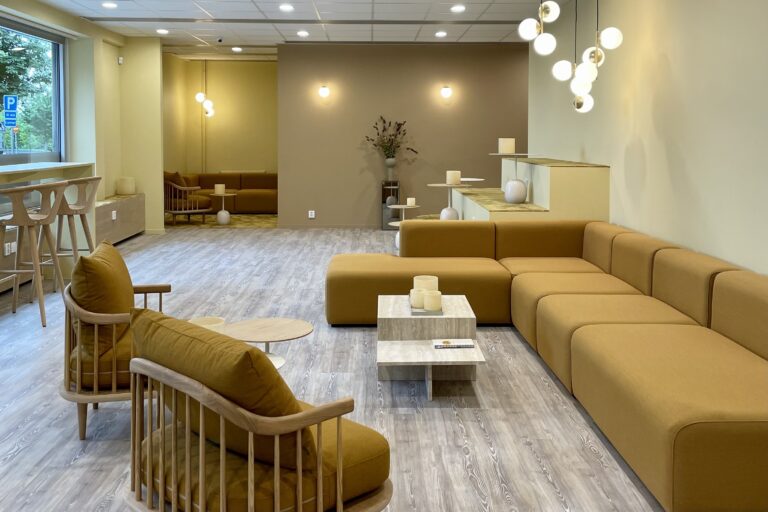 Modern lobby med mjuka gula soffor, trästolar och minimalistiska lampor ger en välkomnande atmosfär.