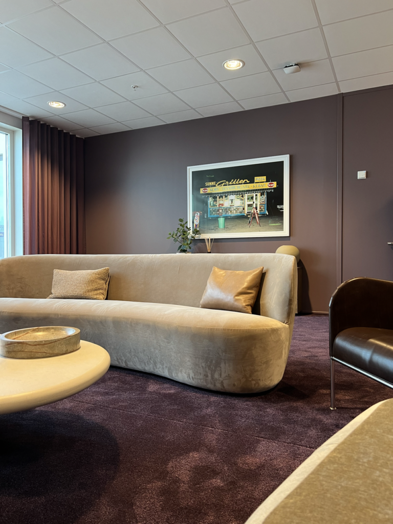 Stilren lounge med en mjuk, beige soffa och lila matta, inrett med minimalistiska accenter och en konstnärlig tavla på väggen.